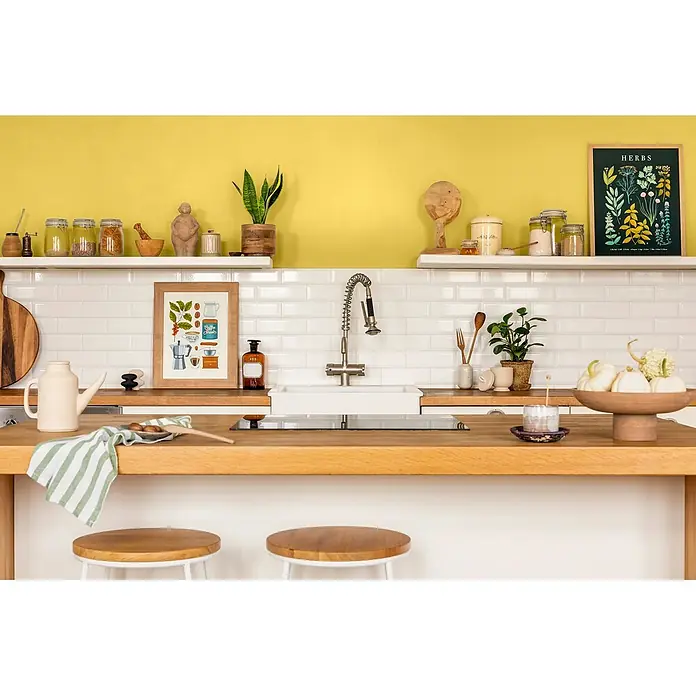 Caleo Color Wandfarbe Lehmfarbe Steppengras - Steppengras, Matt, 5 l - Moderne Küche mit Holzarbeitsplatte, Spüle, Regalen und einer gelben Akzentwand, dekoriert mit Küchenutensilien.