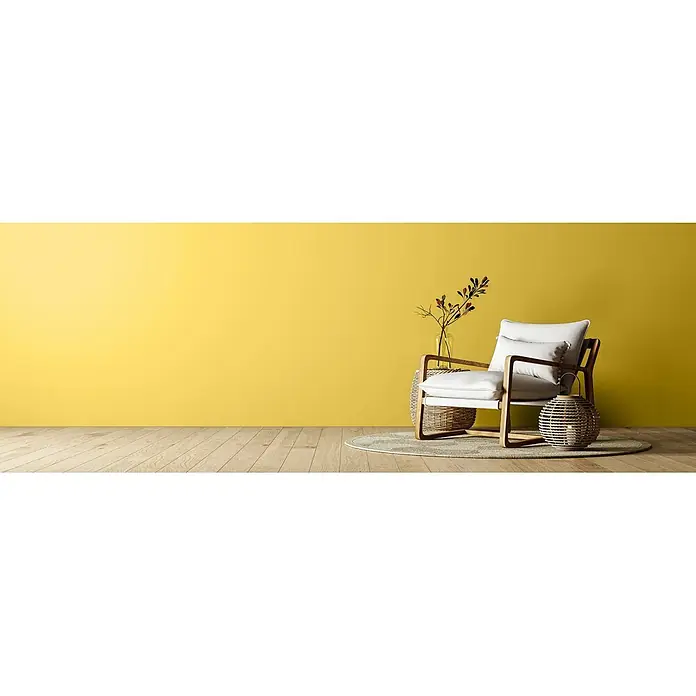 Caleo Color Wandfarbe Lehmfarbe Steppengras - Steppengras, Matt, 5 l - Ein heller Sessel mit Holzrahmen und Korbflechtelementen auf einem Teppich in einem hellen Raum mit gelber Wand.