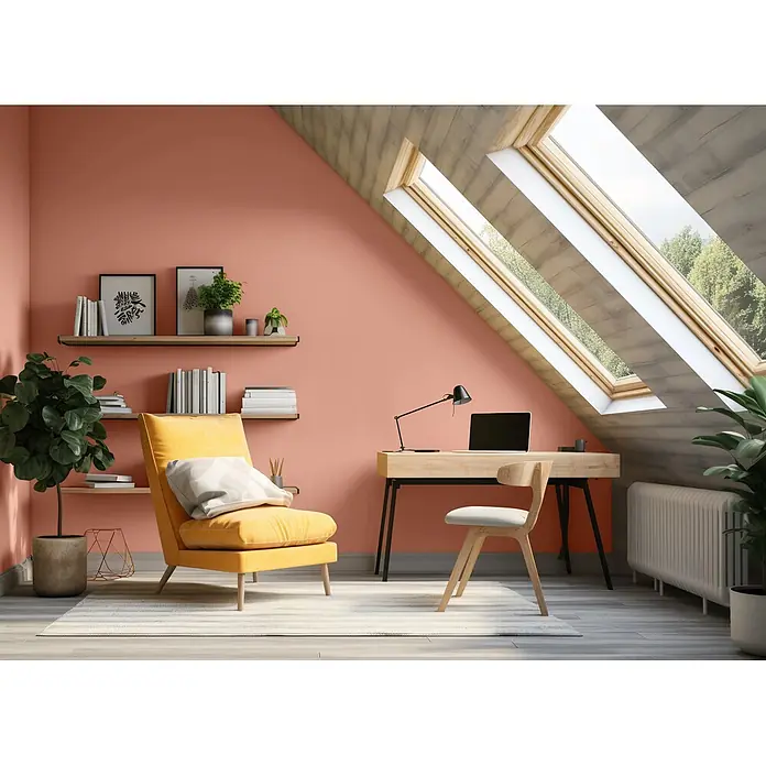 Caleo Color Wandfarbe Lehmfarbe Herbstlaub - Herbstlaub, Matt, 2,25 l - Ein einladendes Dachgeschoss-Home-Office mit warmer oranger Wand, gelbem Sessel, hellem Holzschreibtisch mit Laptop und hellen Dachfenstern.