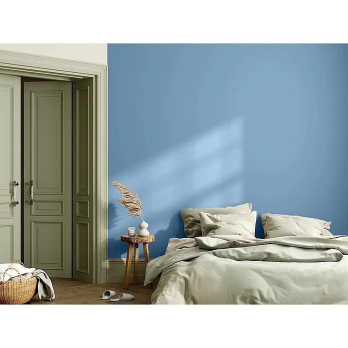 Caleo Color Wandfarbe Lehmfarbe Sommerregen - Sommerregen, Matt, 5 l - Ein Schlafzimmer mit blauer Wand und hellgrünen Türen. Das Bett hat hellgrüne Bettwäsche; ein kleiner Holztisch sorgt für Gemütlichkeit.