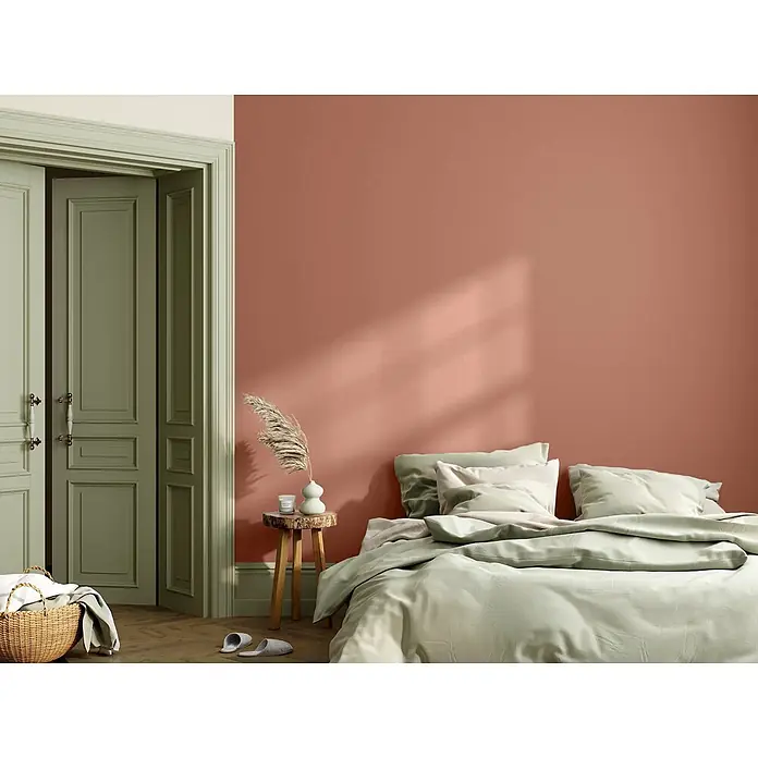 Caleo Color Wandfarbe Lehmfarbe Herbstlaub - Herbstlaub, Matt, 2,25 l - Schlafzimmer mit warmer Terrakotta-Wand und sanfter salbeigrüner Bettwäsche, die eine beruhigende Atmosphäre schafft.