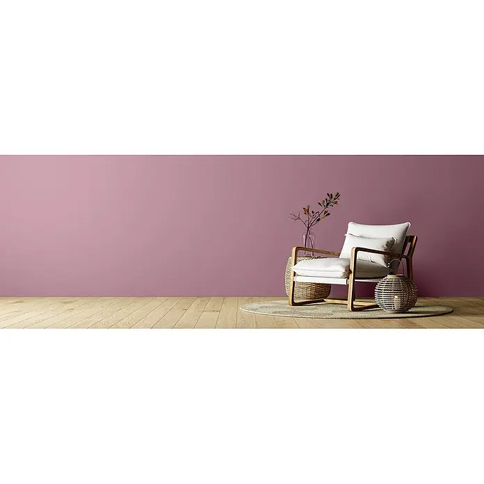 Caleo Color Wandfarbe Lehmfarbe Königsflieder - Königsflieder, Matt, 5 l - Mauve-rosa Wand in einem gemütlichen Raum mit modernem Stuhl, Rattan-Beistelltisch und Naturdekor.
