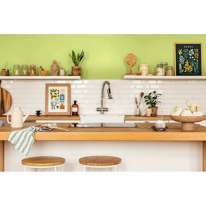 Caleo Color Wandfarbe Lehmfarbe Urzeitfarn - Urzeitfarn, Matt, 5 l - Eine moderne Küche mit Holzarbeitsplatten und weißem Fliesenspiegel, ausgestattet mit Spüle und Barhockern.