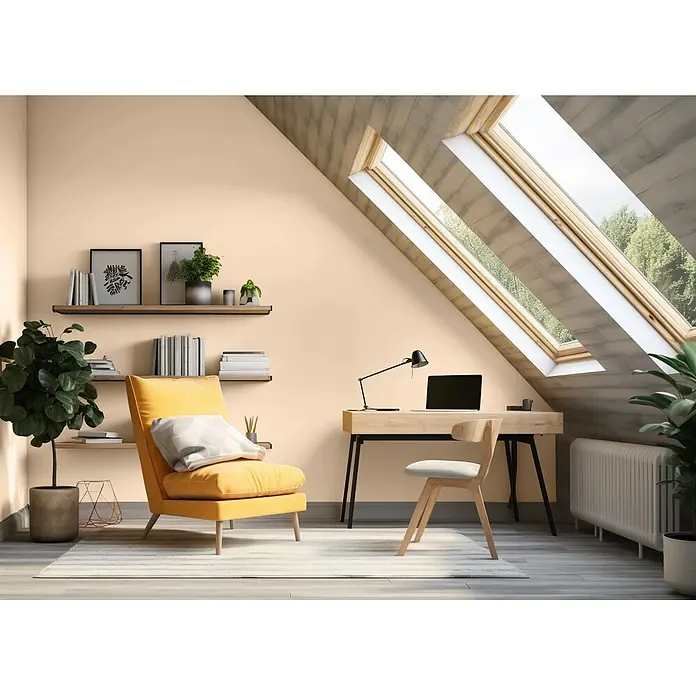 Caleo Color Wandfarbe Lehmfarbe Pampasgras - Pampasgras, Matt, 2,25 l - Ein gemütliches Dachboden-Homeoffice mit pfirsichfarbenen Wänden, Holzmöbeln und einem leuchtend gelben Sessel. Natürliches Licht strömt durch mehrere Dachfenster herein.