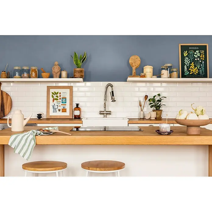 Caleo Color Wandfarbe Lehmfarbe Wolkenbett - Wolkenbett, Matt, 0,15 l - Eine helle, organisierte Küche mit heller Holztheke, weißen Metrofliesen und offenen Regalen mit Küchenutensilien und Deko.