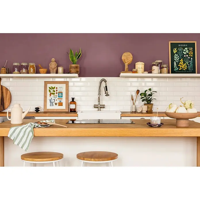 Caleo Color Wandfarbe Lehmfarbe Purpurglöckchen - Purpurglöckchen, Matt, 5 l - Moderne Küche mit heller Holztheke, weißem Waschbecken, U-Bahn-Fliesen und einer lila Akzentwand, dekoriert mit Küchenutensilien.