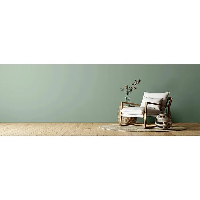 Caleo Color Wandfarbe Lehmfarbe Jura - Jura, Matt, 2,25 l - Moderner Sessel mit weißen Kissen, hellem Holzrahmen, geflochtenem Beistelltisch und Laterne auf einem Teppich.