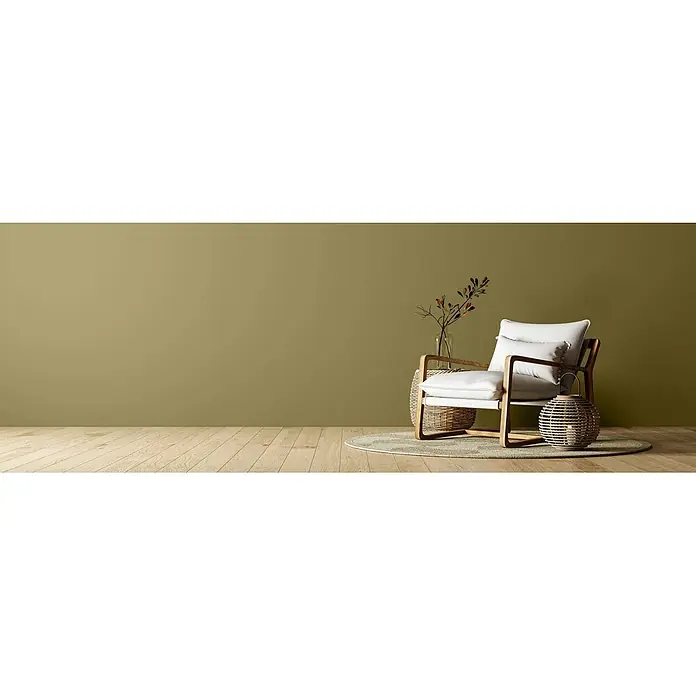 Caleo Color Wandfarbe Lehmfarbe Pistazie - Pistazie, Matt, 0,15 l - Moderner Sessel mit weißen Kissen und Holzrahmen, daneben geflochtener Beistelltisch und Laterne auf rundem Teppich.