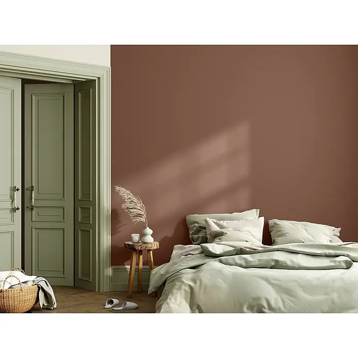 Caleo Color Wandfarbe Lehmfarbe Bärentatze - Bärentatze, Matt, 2,25 l - Schlafzimmer mit rotbraunen Wänden, salbeigrünen Türen und einem Bett mit hellgrünem Bettbezug und Kissen.