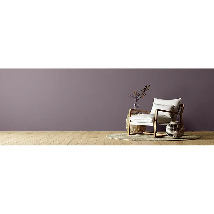 Caleo Color Wandfarbe Lehmfarbe Lavendel - Lavendel, Matt, 2,25 l - Moderner Sessel mit hellem Holzrahmen und weißen Kissen auf einem Teppich, neben Rattantisch und Laterne, vor einer lila Wand.