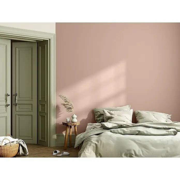 Caleo Color Wandfarbe Lehmfarbe Wüstenwind - Wüstenwind, Matt, 5 l - Ein Bett mit weicher salbeigrüner Bettwäsche in einem gemütlichen Schlafzimmer mit rosafarbenen Wänden und Tageslicht.