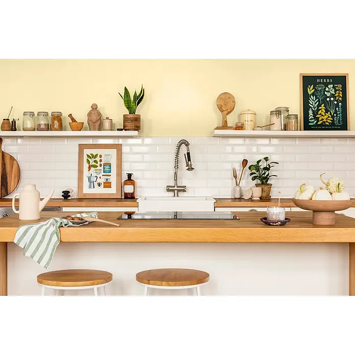 Caleo Color Wandfarbe Lehmfarbe Sandwirbel - Sandwirbel, Matt, 0,15 l - Helle Küche mit Holztheke, weißen Fliesen und gelben Wänden, mit Kochutensilien und Deko.