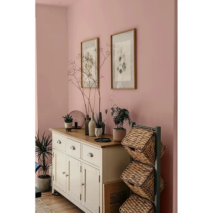 Caleo Color Wandfarbe Lehmfarbe Magnolie - Magnolie, Matt, 0,15 l - Cremefarbenes Holzbuffet mit heller Holzplatte und Metallgriffen, dekoriert mit Pflanzen und Vasen, neben einem Korbregal.