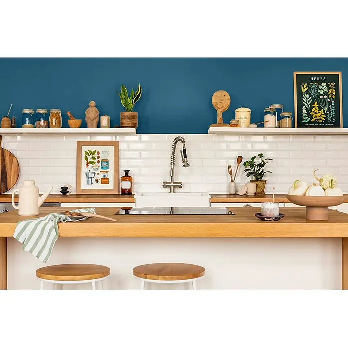 Caleo Color Wandfarbe Lehmfarbe Walgesang - Walgesang, Matt, 5 l - Moderne Küche mit Holztheke, weißen U-Bahn-Fliesen und blauen Wänden, dekoriert mit Pflanzen und Naturelementen.