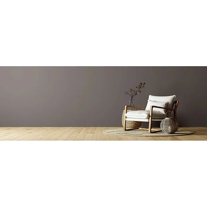 Caleo Color Wandfarbe Lehmfarbe Hochmoor - Hochmoor, Matt, 10 l - Moderner Sessel mit hellem Holzrahmen und weißen Kissen, daneben ein Korbtisch mit Vase und eine Korblaterne, alles auf einem Teppich.