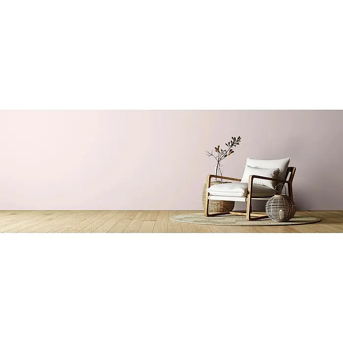 Caleo Color Wandfarbe Lehmfarbe Weidenkätzchen - Weidenkätzchen, Matt, 2,25 l - Heller Sessel mit Holzrahmen und Kissen, begleitet von einem Rattan-Beistelltisch und einer Laterne vor einer zartrosa Wand.