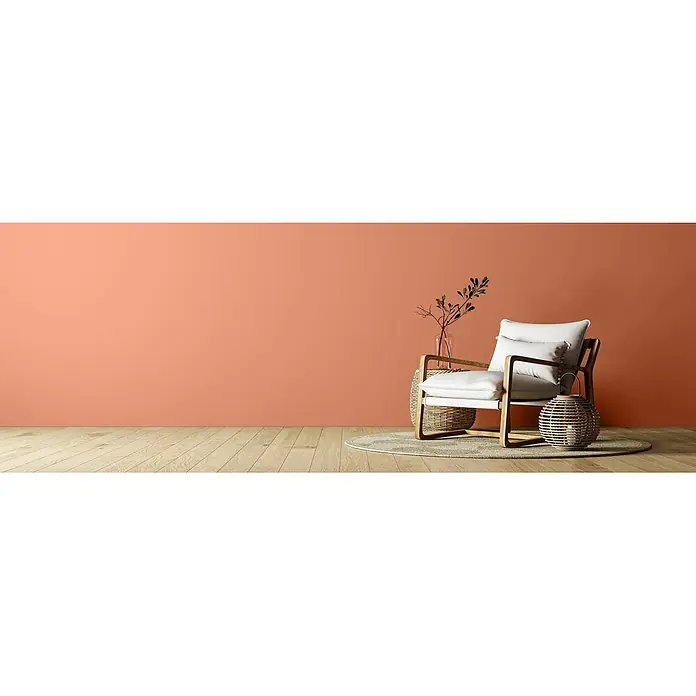Caleo Color Wandfarbe Lehmfarbe Tonscherbe - Tonscherbe, Matt, 0,15 l - Moderner Sessel mit weißen Polstern und Holzrahmen, auf einem Teppich neben Rattantisch und Laterne, vor einer korallenfarbenen Wand.