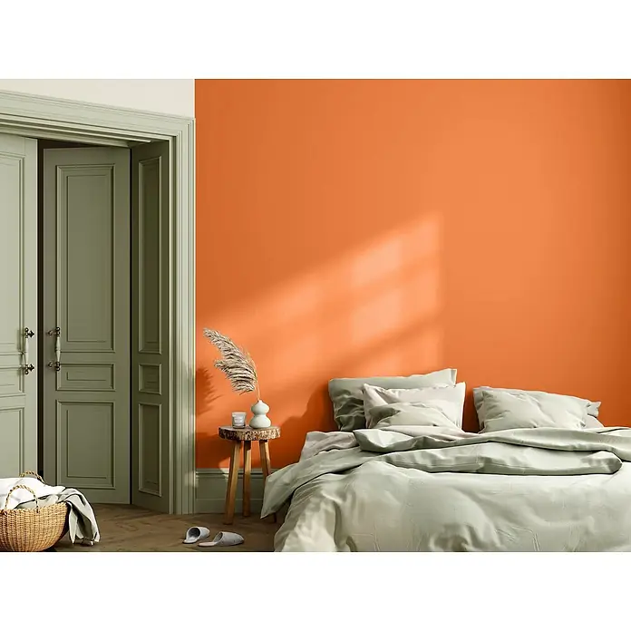 Caleo Color Wandfarbe Lehmfarbe Wüstenfuchs - Wüstenfuchs, Matt, 2,25 l - Hellgrüne Bettwäsche auf einem Bett in einem Schlafzimmer mit warmer orangefarbener Akzentwand.