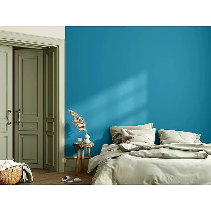 Caleo Color Wandfarbe Lehmfarbe Wellenspiel - Wellenspiel, Matt, 2,25 l - Schlafzimmer mit einer leuchtend blauen Akzentwand, hellbeiger Bettwäsche und salbeigrünen Türen.