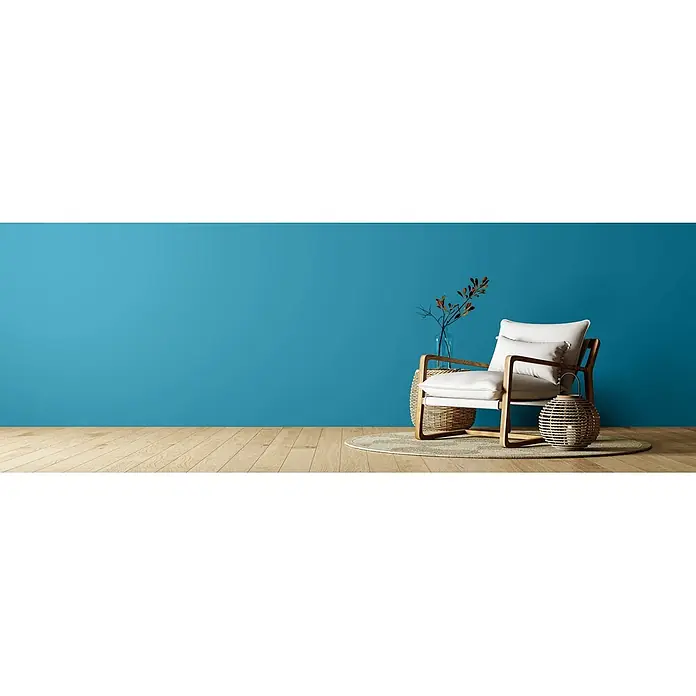 Caleo Color Wandfarbe Lehmfarbe Wellenspiel - Wellenspiel, Matt, 2,25 l - Ein moderner Sessel mit weißen Polstern und hellem Holzrahmen, auf einem Teppich in einem Raum mit blauer Wand. Vase mit Zweigen und Korblaterne daneben.