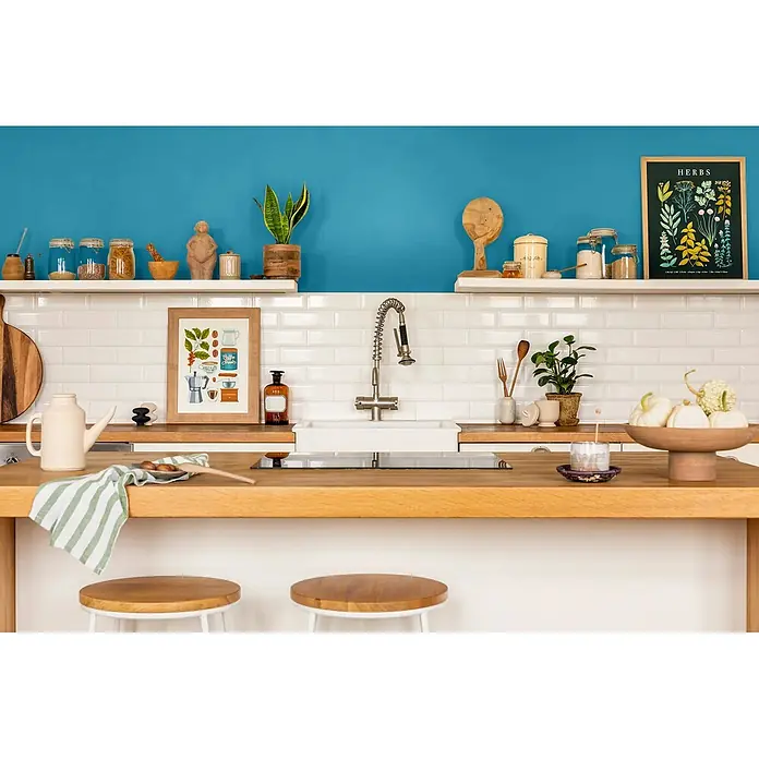 Caleo Color Wandfarbe Lehmfarbe Wellenspiel - Wellenspiel, Matt, 2,25 l - Moderne Küche mit Holztheke, blauer Akzentwand, weißen Metrofliesen und verschiedenen Küchenutensilien und Pflanzen.