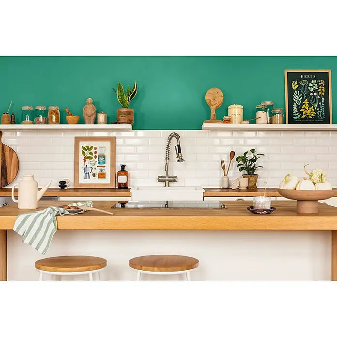 Caleo Color Wandfarbe Lehmfarbe Smaragd - Smaragd, Matt, 0,15 l - Eine moderne Küche mit leuchtend grüner Wand, weißen U-Bahn-Fliesen, Arbeitsplatten und Regalen aus Holz, Spüle, Barhockern und dekorativen Küchenutensilien.