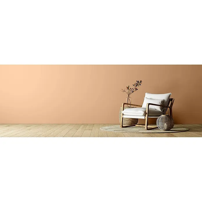 Caleo Color Wandfarbe Lehmfarbe Pfifferling - Pfifferling, Matt, 5 l - Moderner Sessel mit weißen Kissen und Holzrahmen in einem Wohnraum mit pfirsichfarbener Wand und Holzboden.