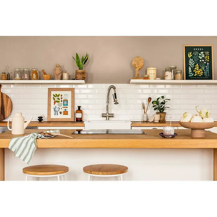 Caleo Color Wandfarbe Lehmfarbe Samtpfote - Samtpfote, Matt, 10 l - Gemütliche Küche mit Holztresen, weißer Fliesenrückwand und offenen Regalen, geschmückt mit Pflanzen und Küchenzubehör.