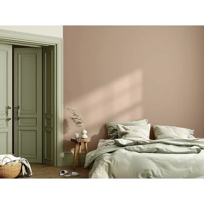 Caleo Color Wandfarbe Lehmfarbe Samtpfote - Samtpfote, Matt, 10 l - Ein gemütliches Schlafzimmer mit altrosa Wänden, salbeigrünen Türen und passender Bettwäsche. Ein rustikaler Holzschemel dient als Nachttisch.