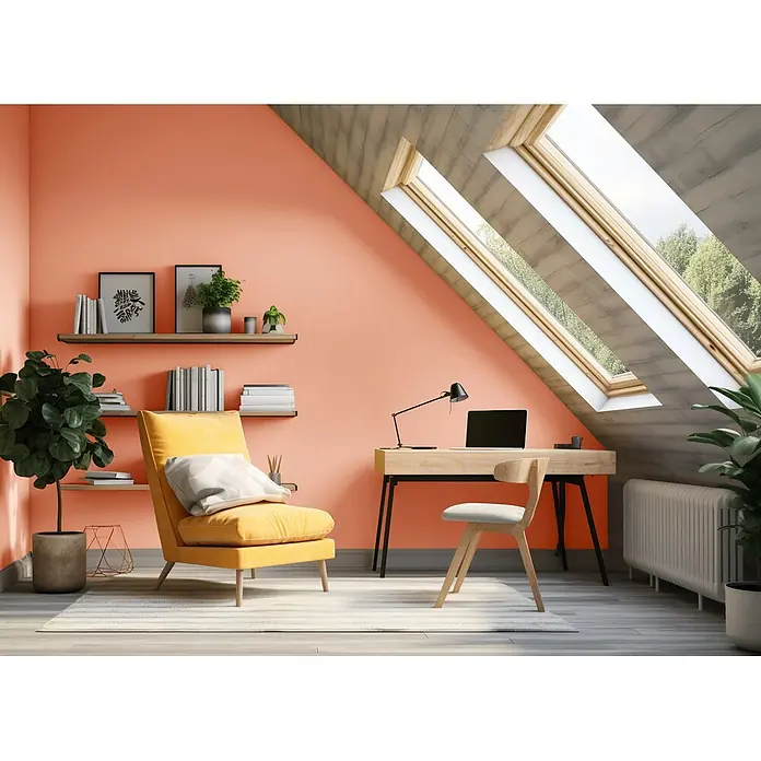 Caleo Color Wandfarbe Lehmfarbe Pfirsichduft - Pfirsichduft, Matt, 5 l - Ein warmes korallenfarbenes Dachboden-Arbeitszimmer mit modernem Holzschreibtisch, Stuhl und gemütlichem gelbem Sessel unter einem Dachfenster.