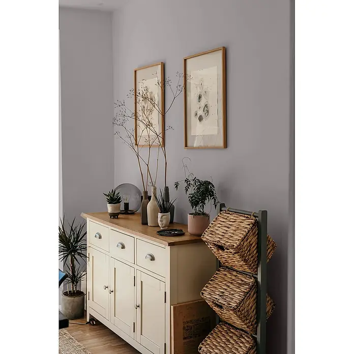 Caleo Color Wandfarbe Lehmfarbe Graureiher - Graureiher, Matt, 0,15 l - Cremefarbenes Holzsideboard mit Naturholzplatte und Metallgriffen, als Stauraum in einem eingerichteten Raum.