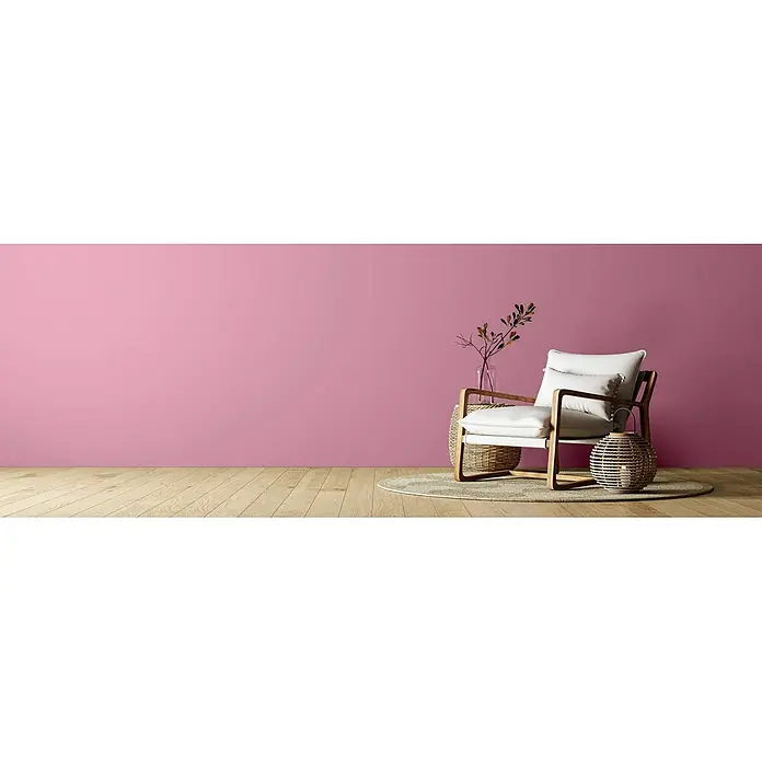 Caleo Color Wandfarbe Lehmfarbe Himbeere - Himbeere, Matt, 2,25 l - Weißer Sessel mit Holzrahmen, Korbtisch und Laterne in einem Raum mit rosa Wand und Holzboden.