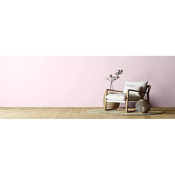 Caleo Color Wandfarbe Lehmfarbe Zuckerwatte - Zuckerwatte, Matt, 2,25 l - Heller Sessel mit Holzrahmen und weißen Kissen, flankiert von natürlichem geflochtenem Beistelltisch und Laterne, auf einem Jute-Teppich.