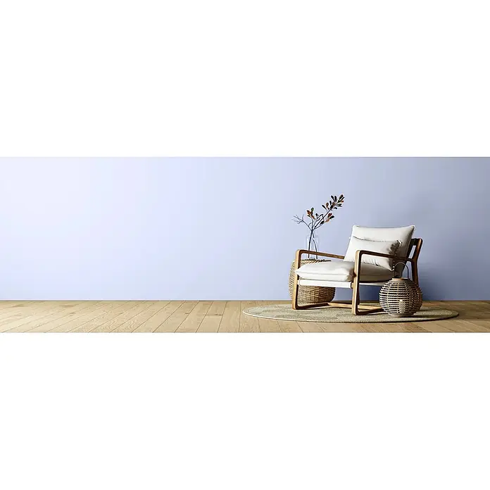 Caleo Color Wandfarbe Lehmfarbe Fliederstrauch - Fliederstrauch, Matt, 2,25 l - Heller Polstersessel mit Holzgestell auf Webteppich vor hellblauer Wand, mit Vase mit Ästen und Weidenlaterne.