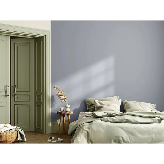 Caleo Color Wandfarbe Lehmfarbe Flusskiesel - Flusskiesel, Matt, 5 l - Ein Schlafzimmer mit lavendelgrauer Wand, salbeigrünen Kassettentüren und einem Bett mit hellgrüner Bettwäsche. Warmes Licht fällt herein.