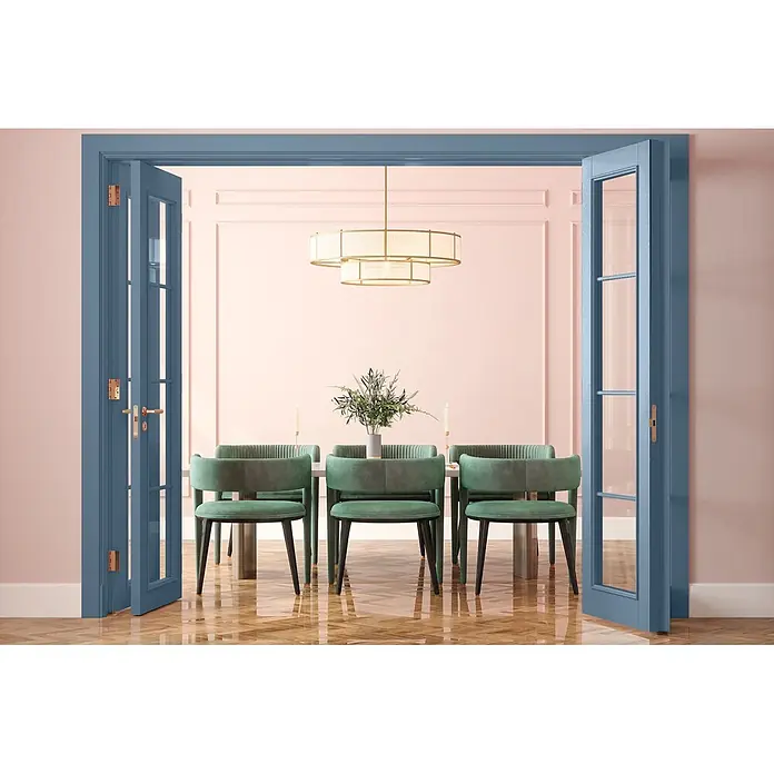 Caleo Color Buntlack Morgennebel - Morgennebel, Seidenmatt, 0,68 l, Wasserbasiert - Elegantes Esszimmer mit rosa Wänden, grünen Samtstühlen, hellem Holztisch und einem Kronleuchter, durch blaue Flügeltüren gesehen.