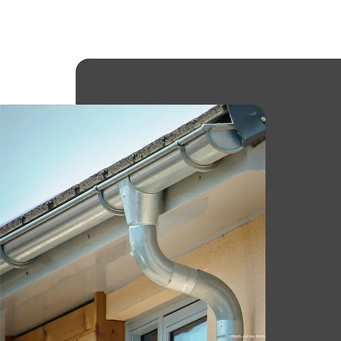 Zambelli Dachrinne Rohrschelle DN 100 /M10 verzinkt mit Gewindemuffe Silber - Nennweite: 120 mm, Länge: 3 cm, Stahl, Silber - Silbergraues Metall-Dachrinnensystem mit Fallrohr an einem Gebäude zur Regenwasserableitung.