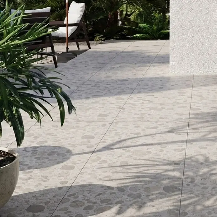 Feinsteinzeugfliese Vogue - 60 x 60 cm, Sand, Matt - Helle beigefarbene Terrassenfliesen mit unregelmäßigem Steinmuster als Bodenbelag im Garten mit Möbeln und Pflanzen.