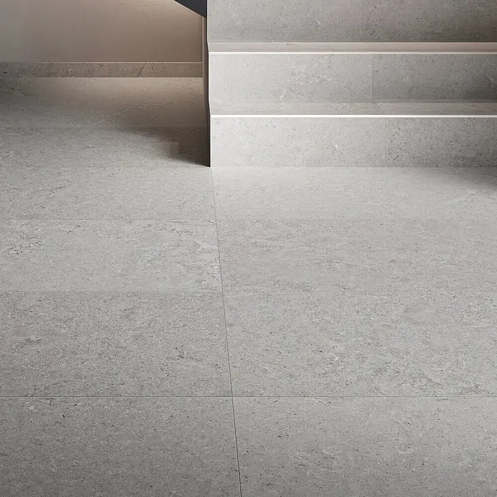 RAK Ceramics Valdi Stufen- & Abdeckplatte - 60 x 30 cm, Taupe, Unglasiert - Graue Fliesen in Steinoptik bedecken den Boden und eine Treppe in einem modernen Interieur.