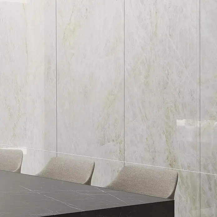 RAK Ceramics Feinsteinzeugfliese Crystal - 60 x 120 cm, Onyx White, Glänzend - Teil eines dunkelgrauen Marmortisches mit hellbeigen Polsterstühlen in modernem Ambiente.