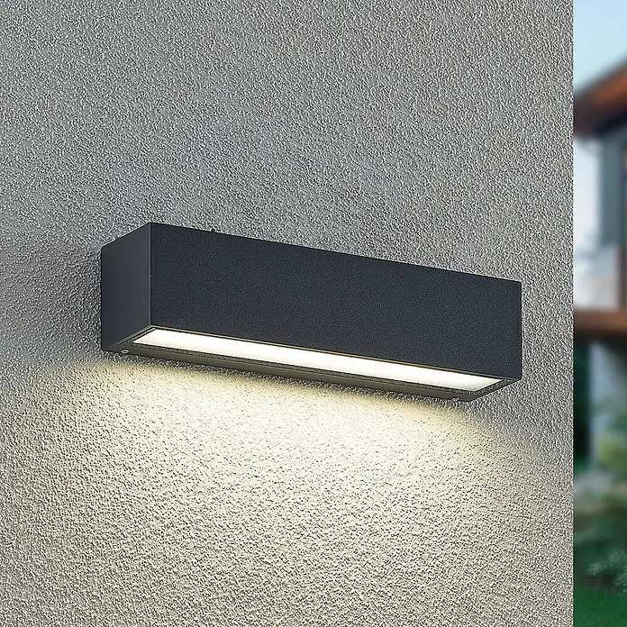 Arcchio LED Wandleuchte aussen in anthrazit, Aussenlampe Wand -  - Dunkelgraue rechteckige Outdoor-Wandleuchte an einer strukturierten Wand, die warmes Licht nach unten abgibt.