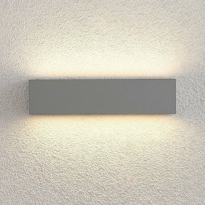 Lucande LED Wandleuchte aussen in silber, Aussenlampe Wand -  - Rechteckige graue Wandleuchte auf einer strukturierten Wand, die warmes Licht nach oben und unten abgibt.