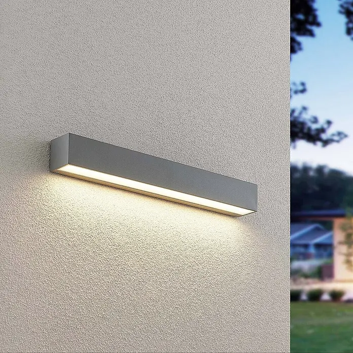 Lucande Außenwandleuchte Lengo - alu / grau / zink, IP65 - Graue, rechteckige Außenwandleuchte an einer strukturierten Wand, die warmes Licht nach unten strahlt.