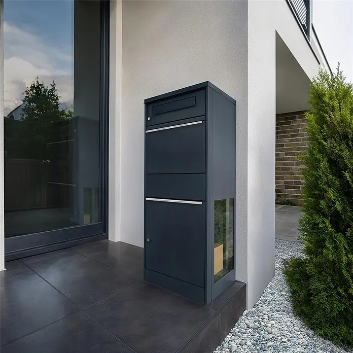 Metzler Paketbox BRFK BISPO SF - L x B x H: 37 x 50,2 x 112 cm, Anthrazit, Stahl, Paketfach, Mit Seitenfenster - Dunkelgrauer Paketbriefkasten mit Briefschlitz, mehreren Fächern und einer Glasscheibe mit Paket, am Hauseingang platziert.