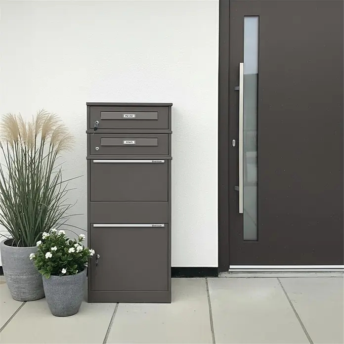 Metzler Paketbox 2 BRFK BISPO RE - L x B x H: 37,4 x 50,3 x 130,3 cm, Eisenglimmer, Stahl, Paketfach, Mit 2 Briefkastenfächern und Namensschildern - Dunkelgraues Mehrparteien-Briefkastensystem mit mehreren Fächern, neben einer modernen Tür.