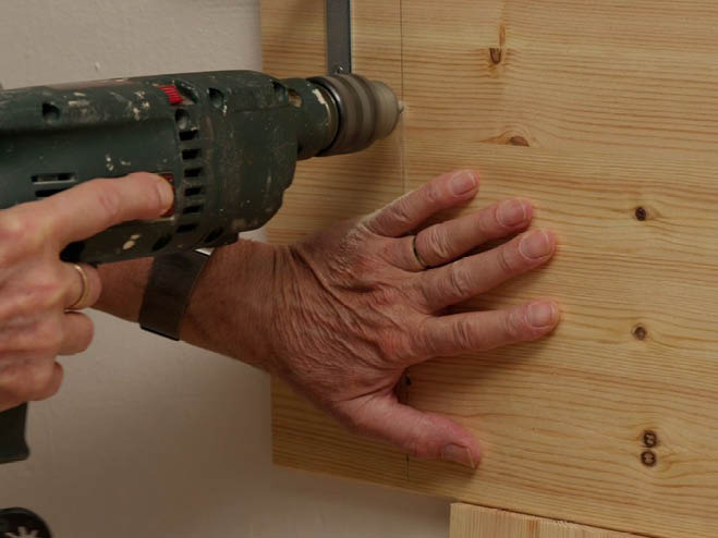 Holzplatte wird mit dem Bohrer an die Wand geschraubt