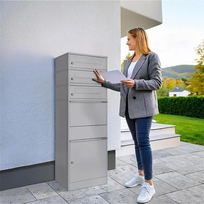 Metzler Paketbox 3 BRFK BISPO - L x B x H: 37,4 x 50,3 x 147,7 cm, Graualuminium, Stahl, Paketfach, 3 Briefkastenfächer - Hoher grauer Mehrfach-Briefkasten an einer Hauswand, eine Frau interagiert damit.