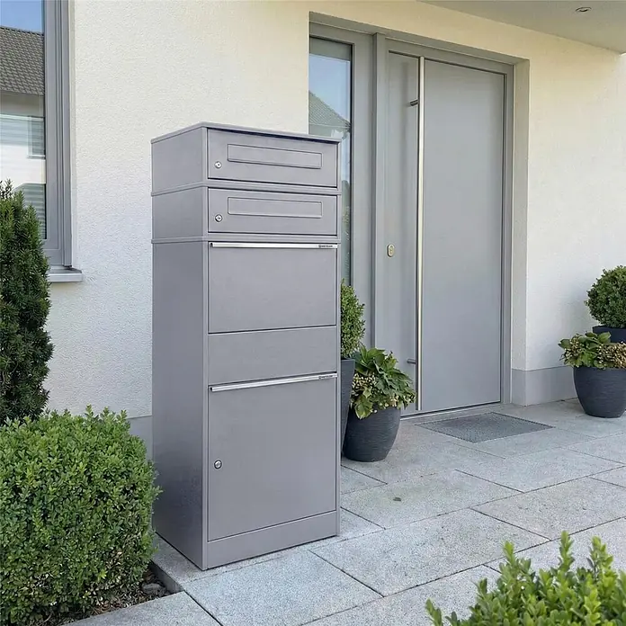 Metzler Paketbox 2 BRFK BISPO - L x B x H: 37,4 x 50,3 x 130,3 cm, Graualuminium, Stahl, Paketfach, 2 Briefkastenfächer - Hoher grauer Metall-Brief- und Paketkasten neben einem modernen Hauseingang mit mehreren Fächern.