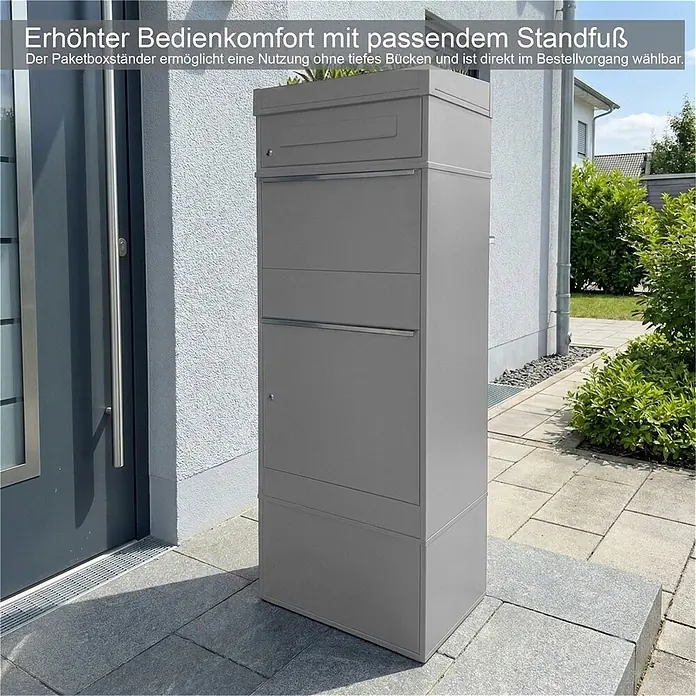 Metzler Paketbox BRFK PD BISPO - L x B x H: 37,4 x 50,3 x 119,9 cm, Graualuminium, Stahl, Paketfach, Mit Pflanzdach - Grauer Paketbriefkasten mit erhöhtem Standfuß für bequeme Nutzung ohne Bücken, platziert vor einem Haus.