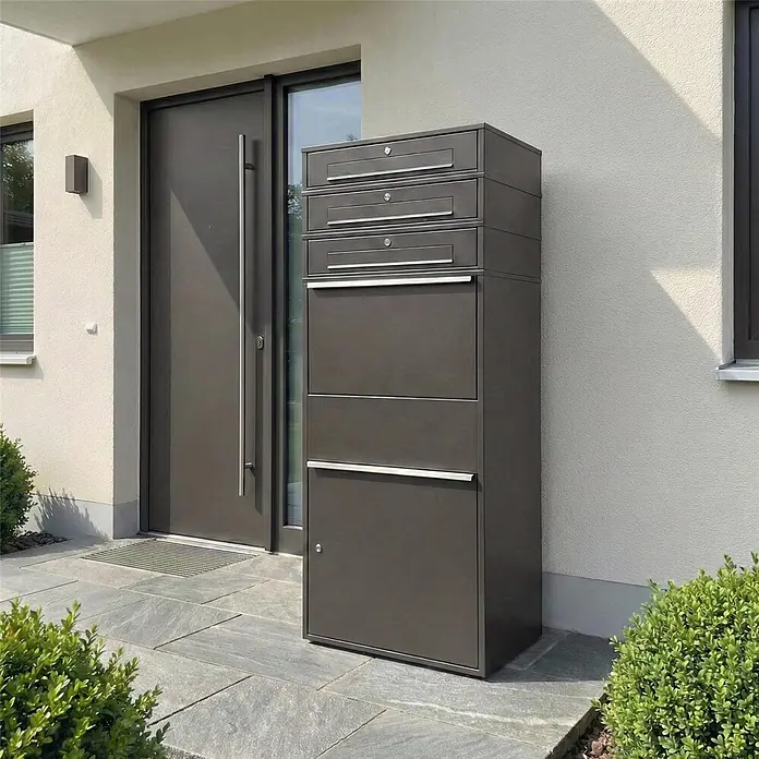 Metzler Paketbox XL 3 BRFK MAX - L x B x H: 45 x 72 x 177 cm, Eisenglimmer, Stahl, Paketfach, 3 Briefkastenfächer - Dunkelgraue Briefkasten- und Paketbox-Kombination neben einer modernen Haustür.